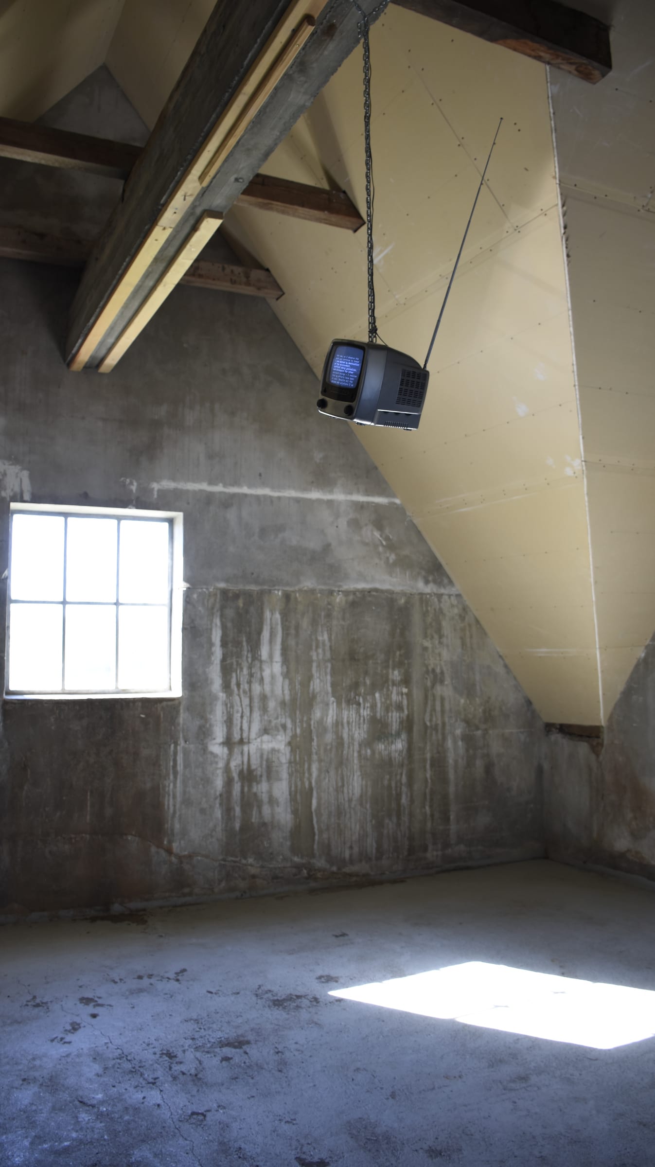 The television suspended beside a window in the concrete gallery