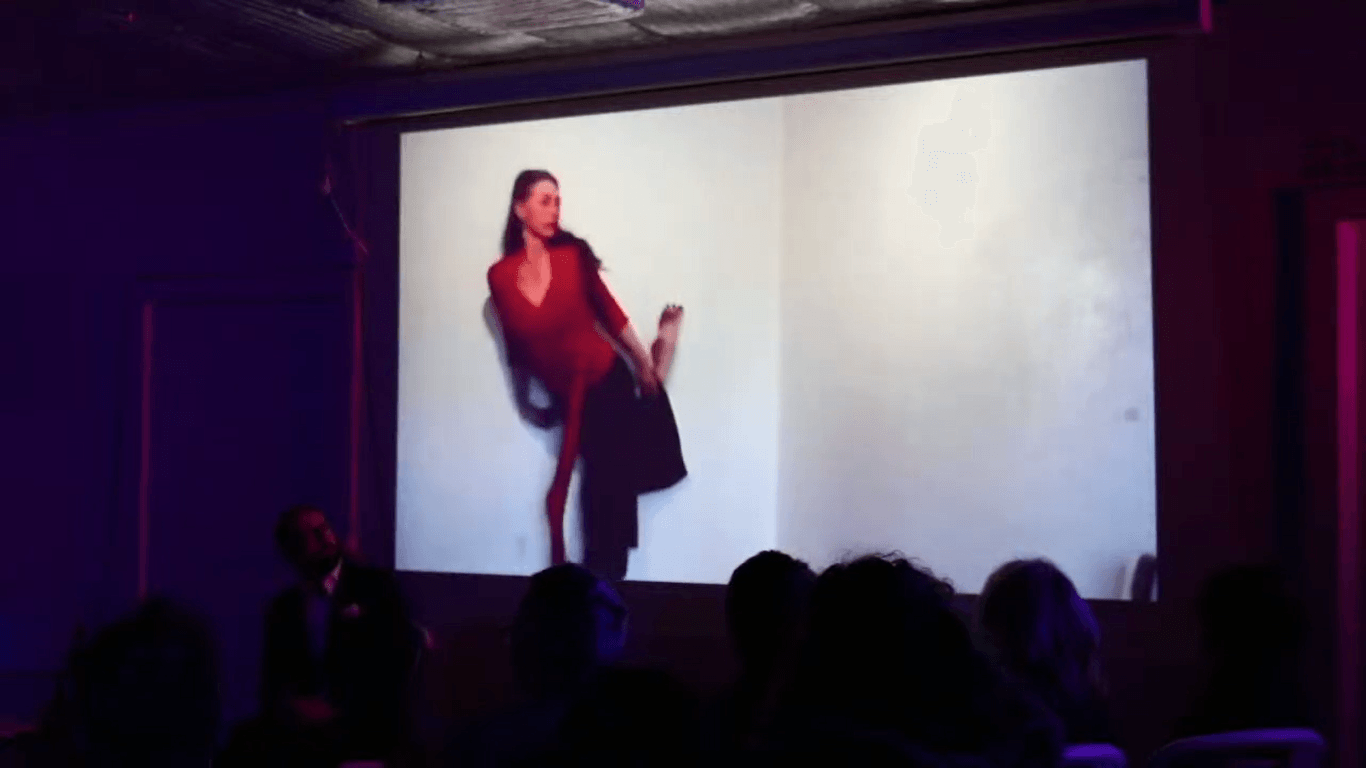 A projected dancer in a red top on a large screen in a dark room