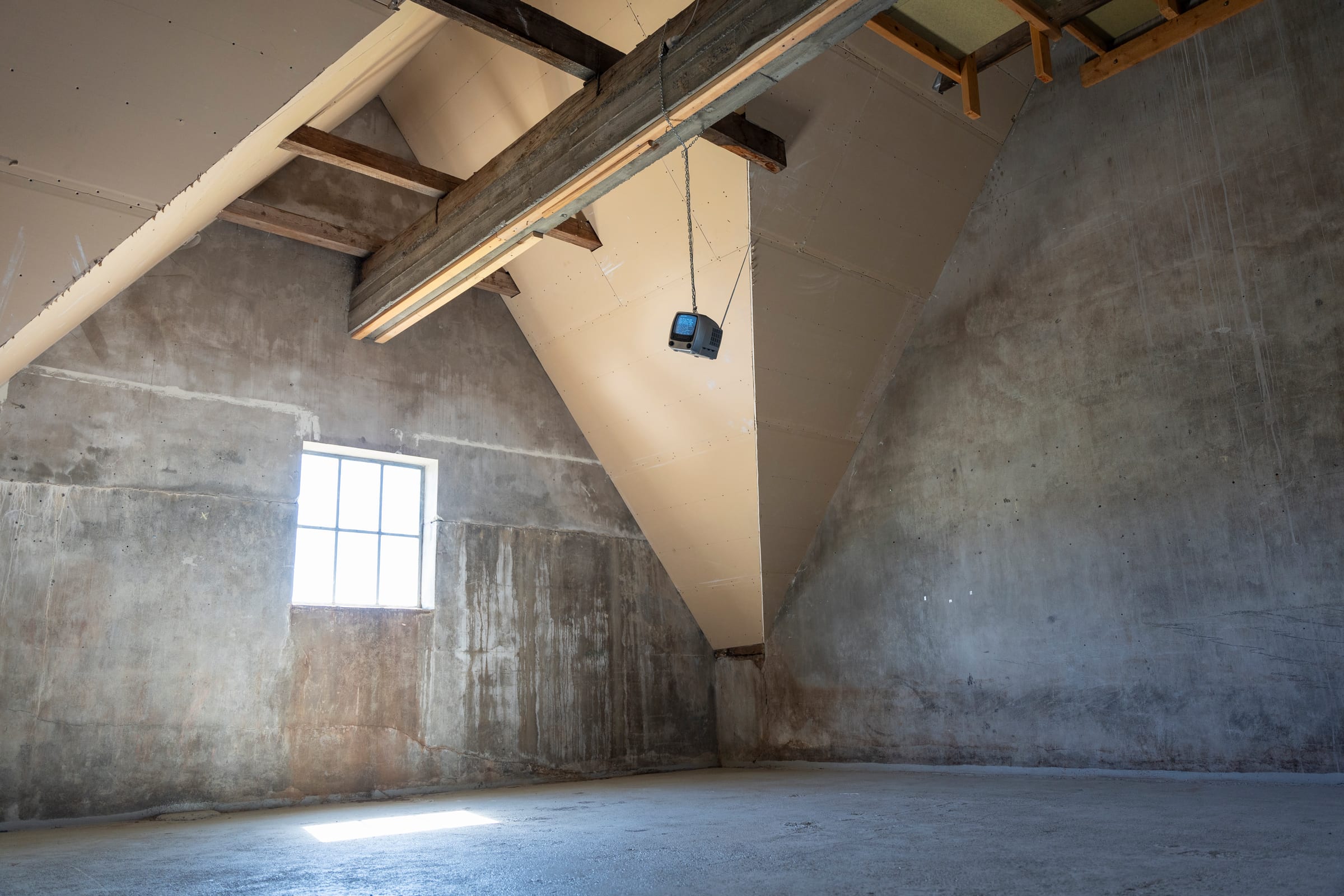 The CRT television hanging from the rafters of a concrete room with a sloped roof at SÍM Korpúlfsstöðum, Reykjavík